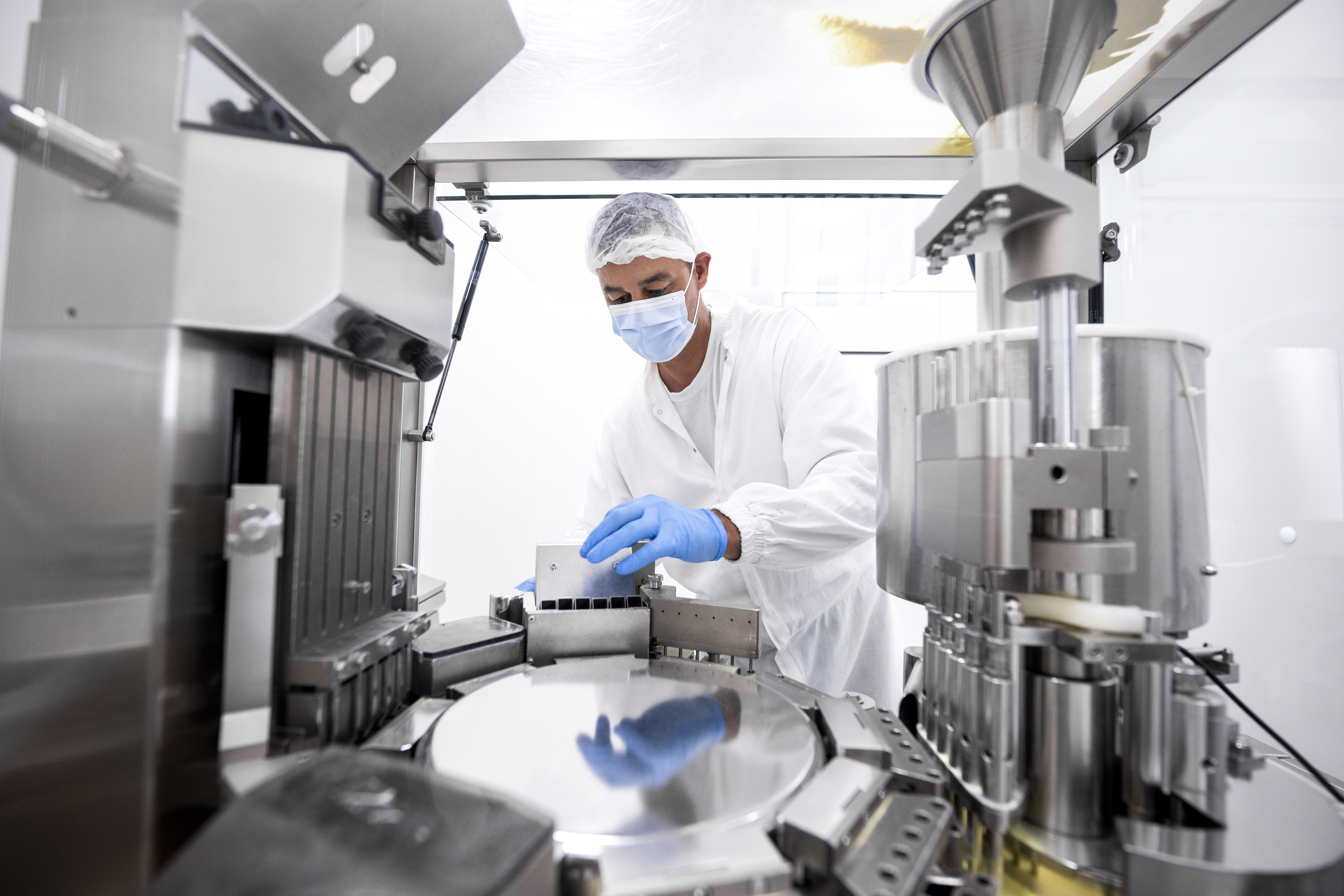 Pharmaceutical technician in a protective clothing equipment seen in a laboratory during a manufacturing process