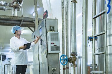 Factory technician inspecting an industrial tank with a clipboard, showcasing precision, quality control, and attention to detail in a modern manufacturing environment.